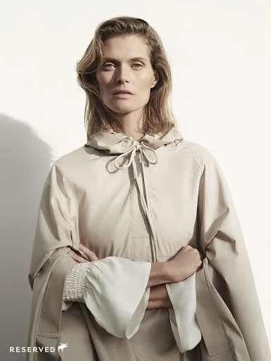 Model in a beige hooded cape with ruffled cuffs