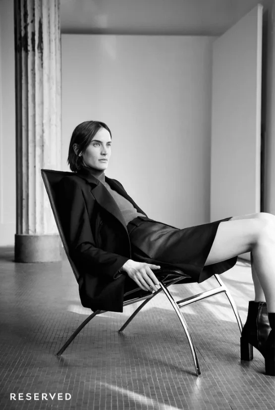 Model in a black jacket and mini skirt on a lounge chair, black and white