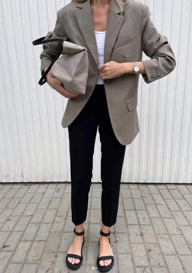 Model in a grey blazer carrying a soft leather clutch