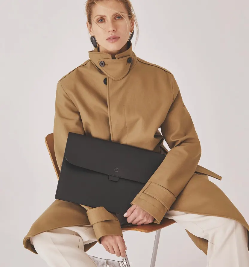 Model in a camel coat holding a black leather folio clutch