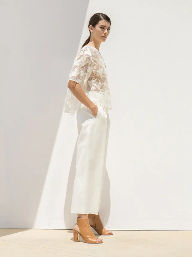 Model in a white lace top and wide white trousers